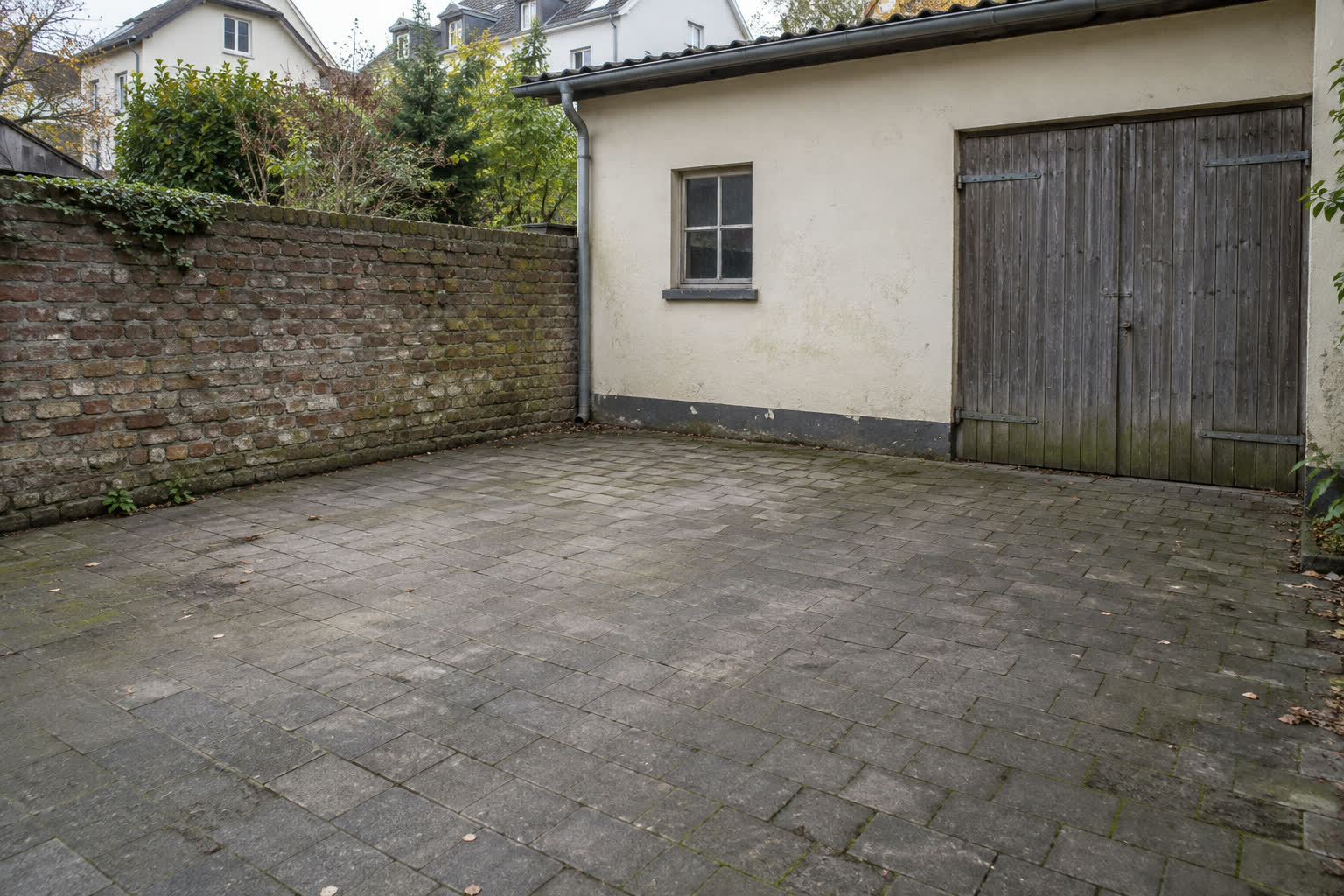 Geräumter Hinterhof eines abgeschlossenen Auftrags: freies Pflaster vor Garage und Mauer
