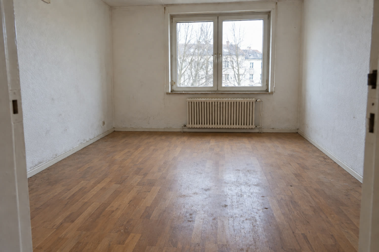 Derselbe Raum leer geräumt: Dielenboden, Heizkörper unter dem Fenster, freie Wände